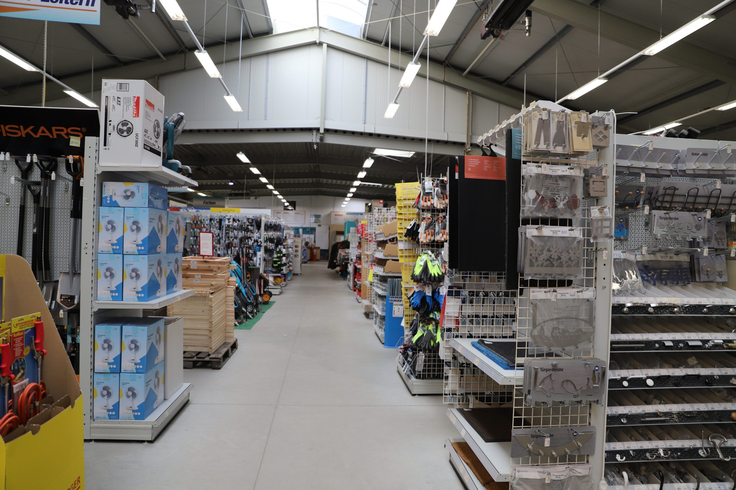 Ein heller Baumarktgang zeigt gut sortierte Regale mit Baustoffen und Werkzeugen für Innenausbau und Gartenprojekte.