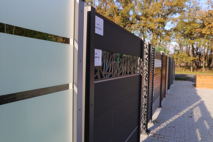 Eine Auswahl an Sichtschutzzäunen aus verschiedenen Materialien wird im Freien auf einem gepflasterten Weg präsentiert.